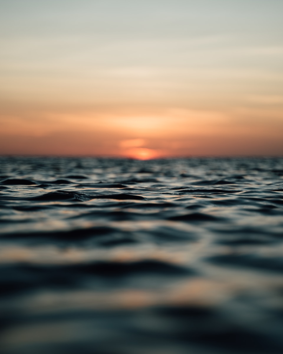 The sun is setting over the horizon of the ocean